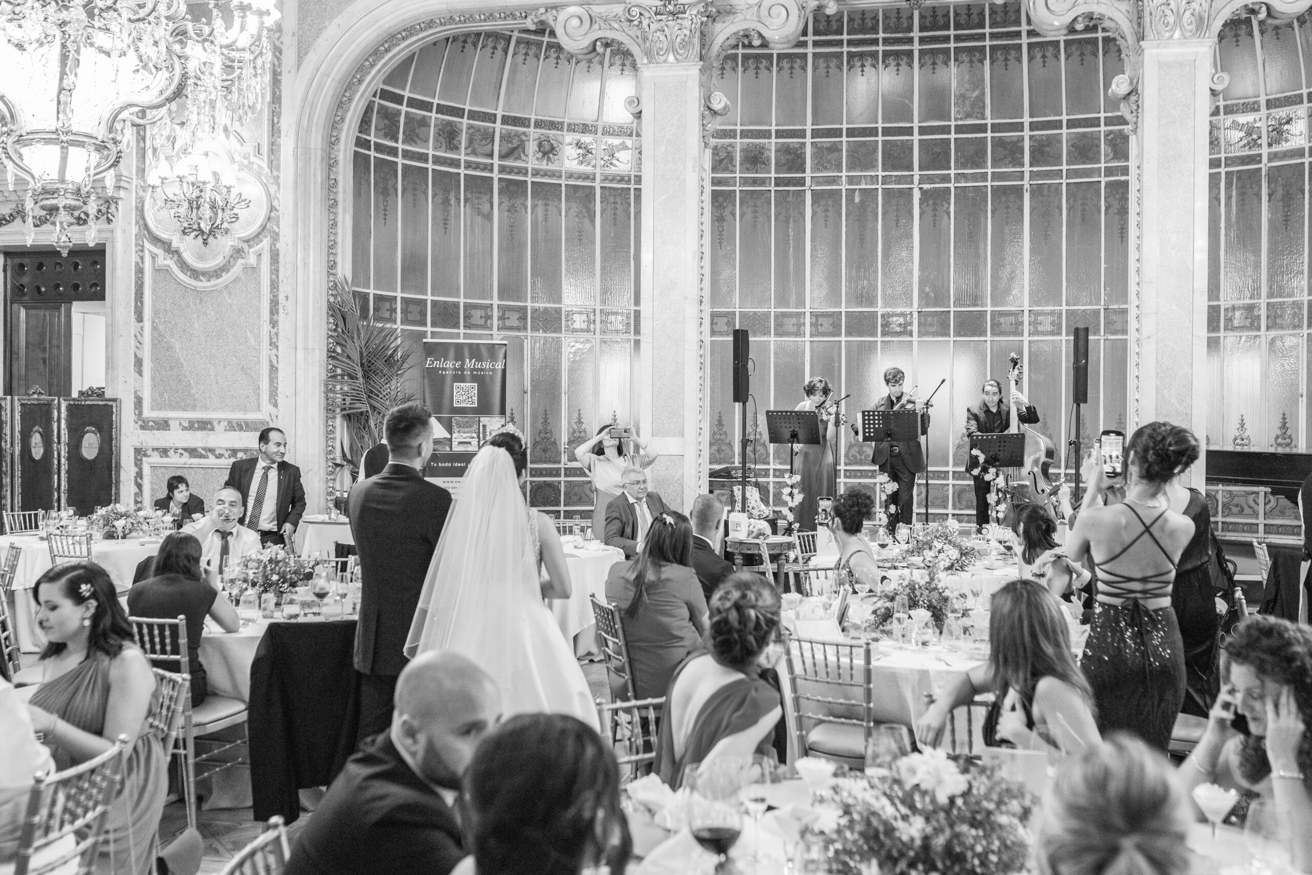 Trío de cuerda amplificado tocando en banquete de boda, novios emocionados mirándoles mientras disfrutan de la música en vivo.